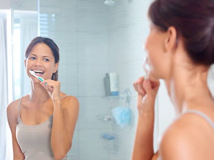 Lächelnde Frau beim Zähneputzen. Hier lesen: Zahnfleisch gesund halten.