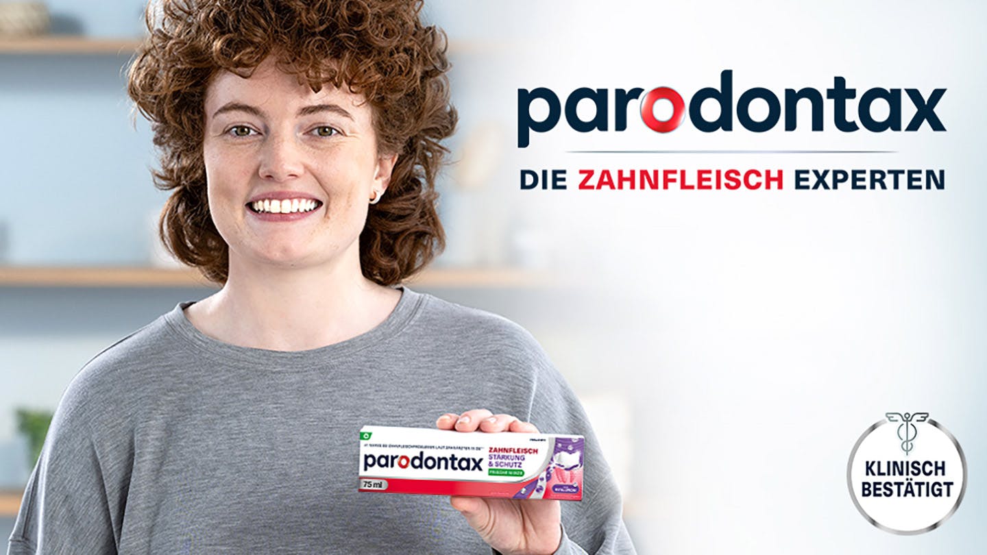 Frau hält eine Packung parodontax Zahnfleisch Stärkung & Schutz Zahnpasta, die klinisch bestätigt ist.​
