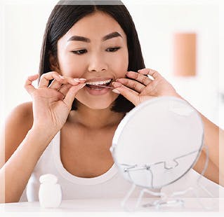 woman looking in the mirror using dental floss