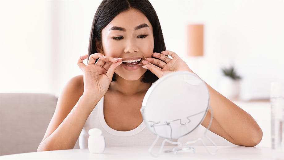 woman looking in the mirror using dental floss