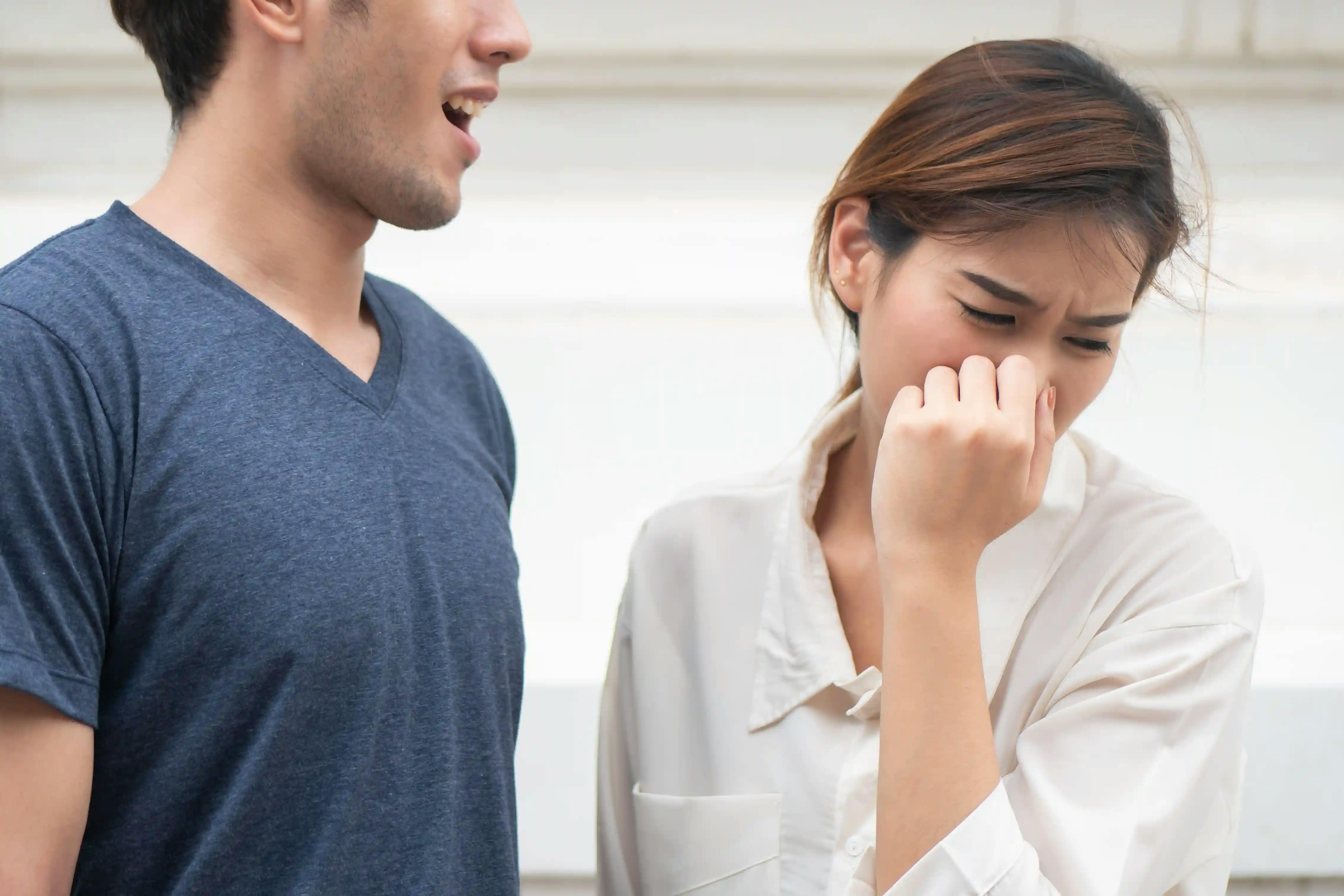 Woman covers her nose and turns away from man with bad breath