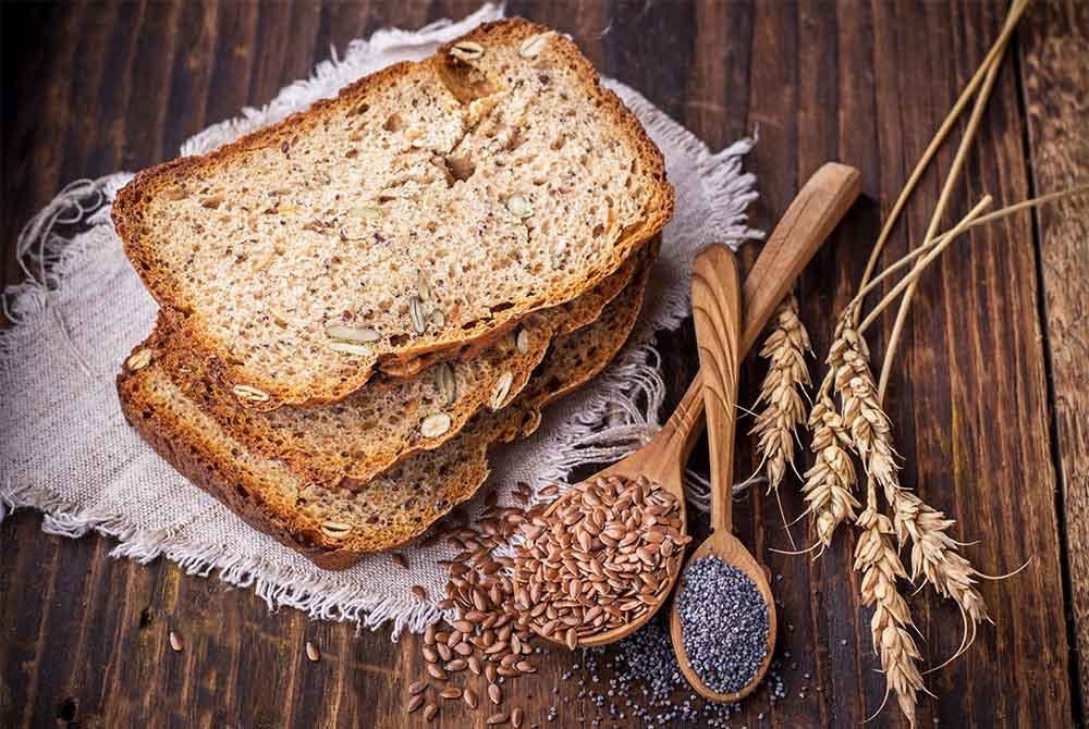 Bread slices with spoons of seeds on dark wooden background