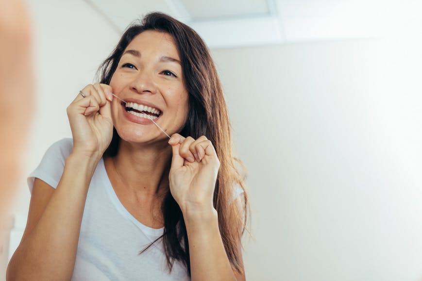 Woman looks in the mirror while flossing her teeth