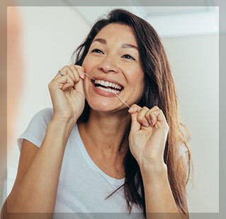 Woman looks in the mirror while flossing her teeth