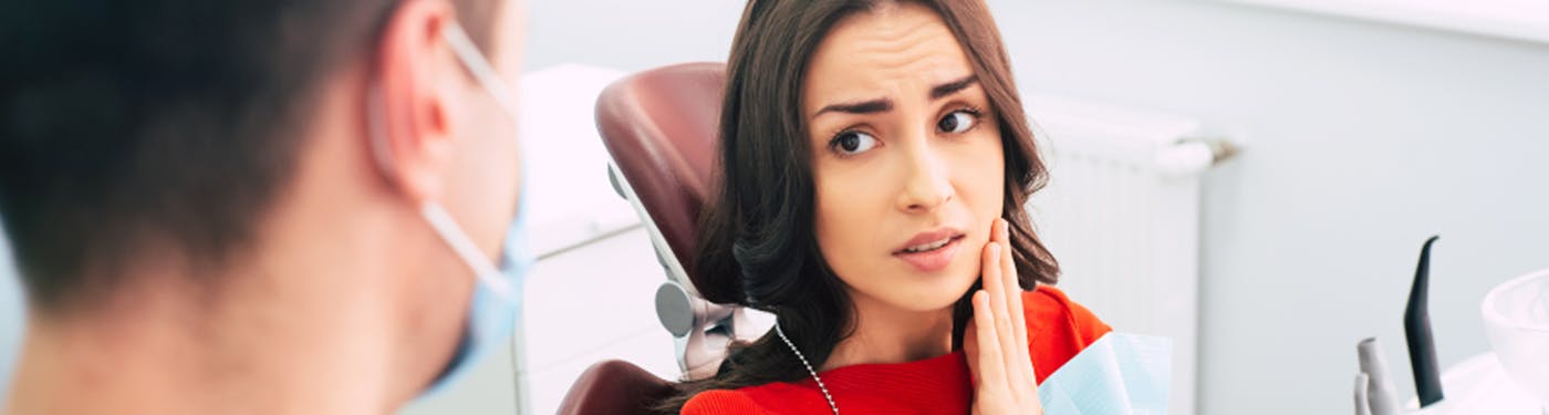 Woman looking at dentist while holding jaw 