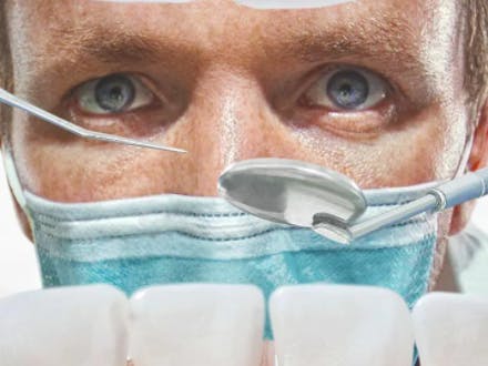 Manlig tandläkare undersöker mun med verktyg