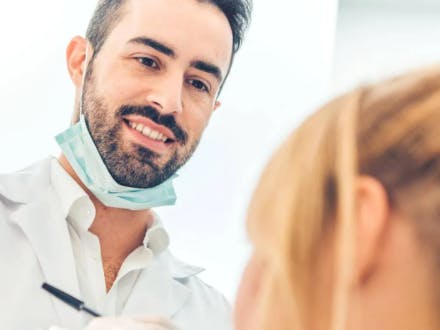 Manlig tandläkare pratar med kvinnlig patient