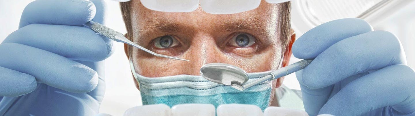 Manlig tandläkare undersöker mun med verktyg