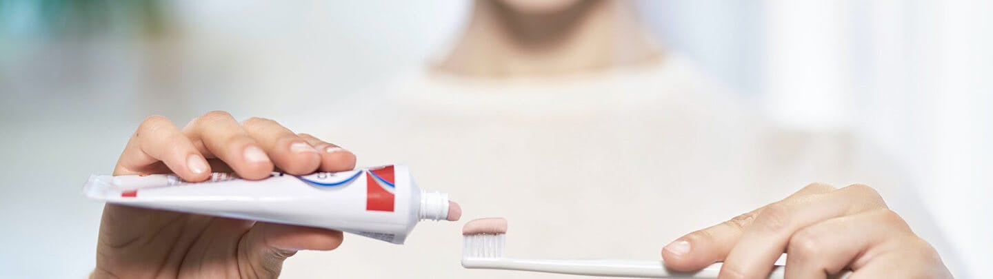Kvinna i beiege långärmad tröja applicerar Parodontax tandkräm på sin tandborste