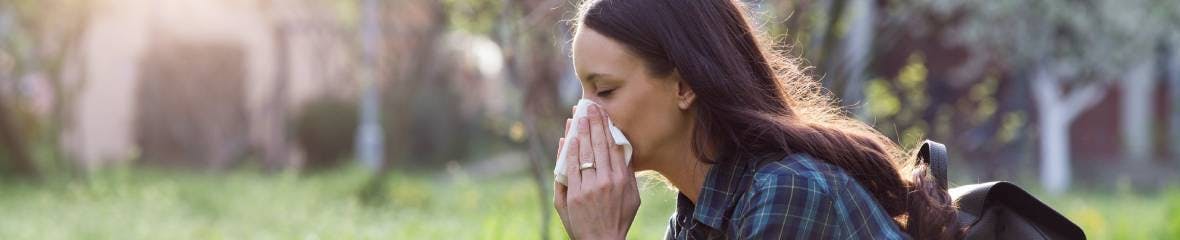 Woman outside in a field blowing nose, allergies