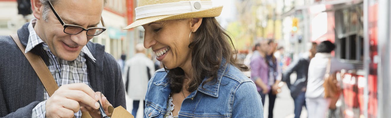 Man and woman smiling on sidewalk of busy street 