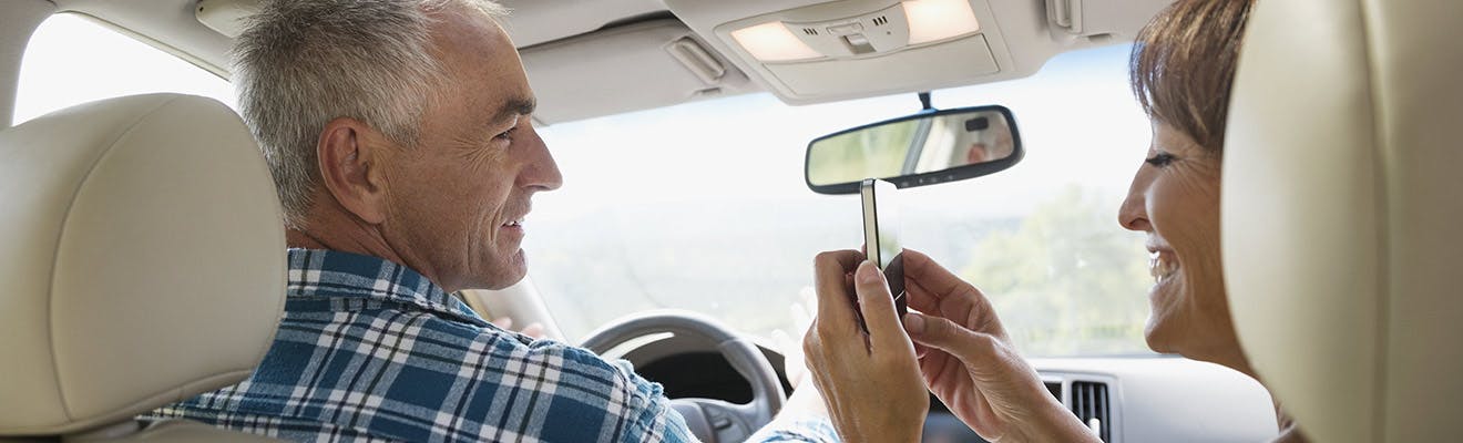 Older couple in a car and taking a picture of mans smile with dentures