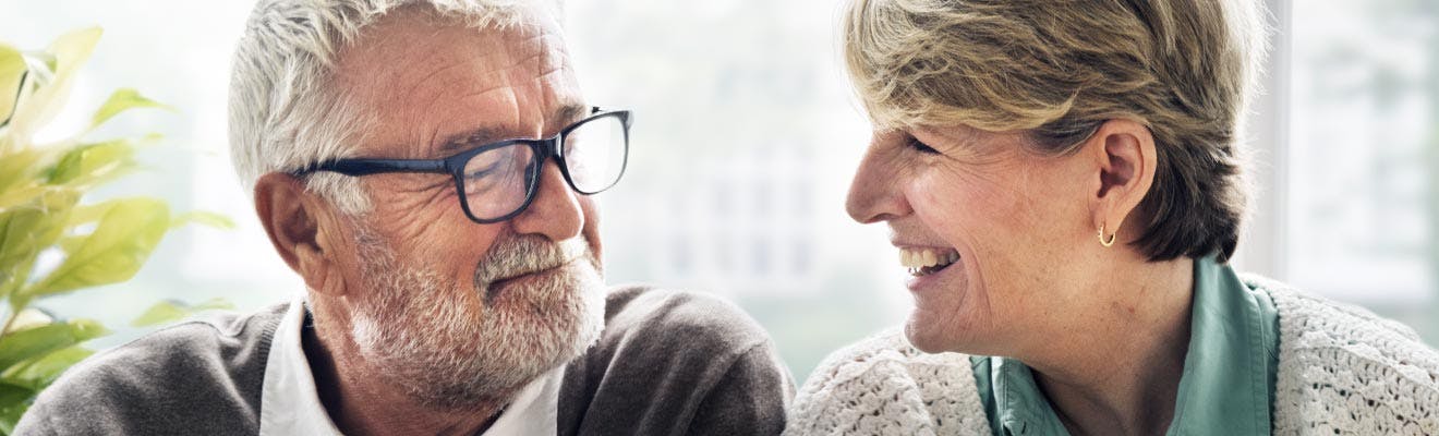 pareja adulta mayor viendose mutuamente y sonriendo gracias a corega