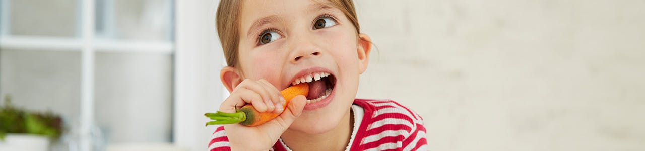 Young girl biting into a carrot