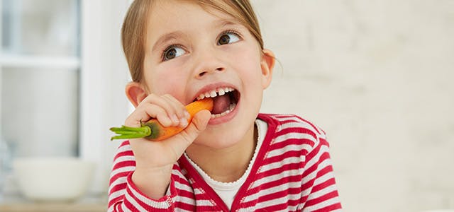 Young girl biting into a carrot