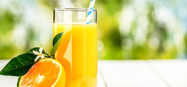 Glass of orange juice and half of an orange on a deck