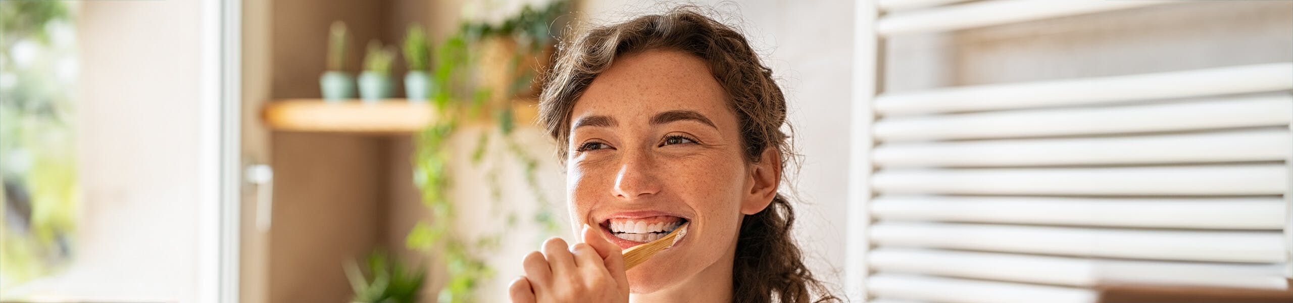 Smiling Young Woman Brushing Teeth In Bathroom