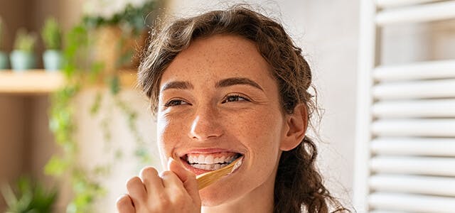 Smiling Young Woman Brushing Teeth In Bathroom