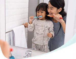 Woman and child brushing teeth in mirror