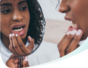 Woman looking at teeth with a handheld mirror 