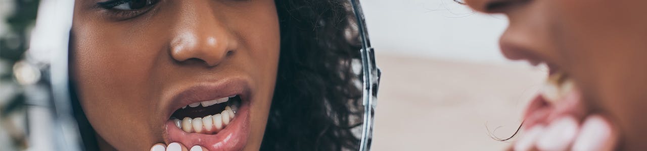 Woman looking at teeth with a handheld mirror