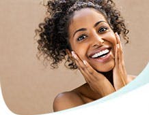 A young black woman is smiling with her hands on her cheeks.