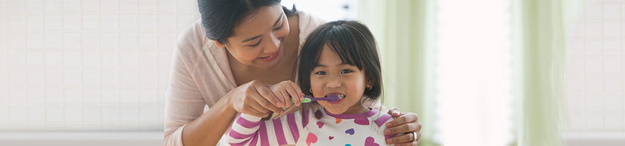 Une mère aide sa fille à se brosser les dents devant le miroir avec Pro-Émail® 