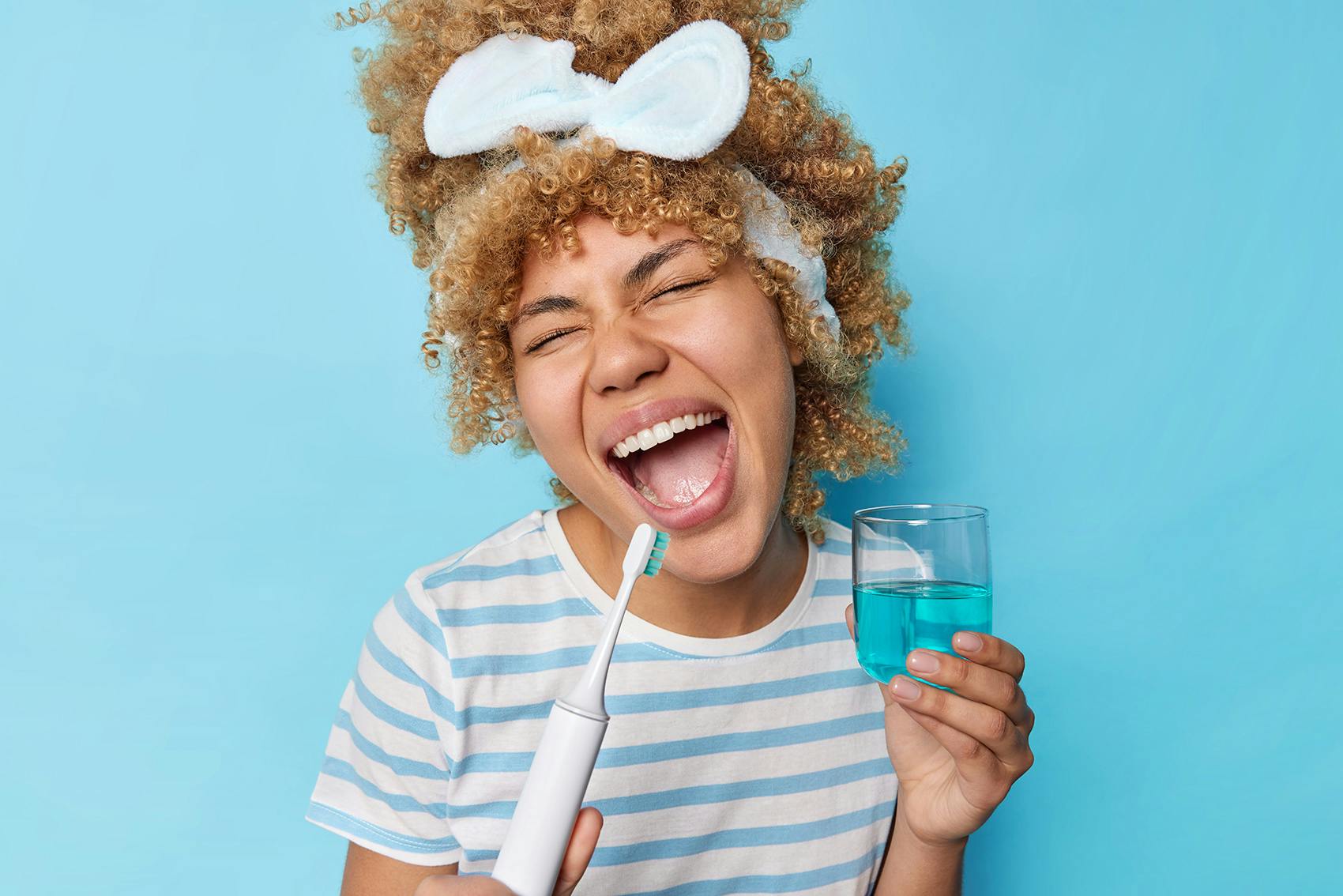 Smiling woman holding a toothbrush and a cup of mouthwash