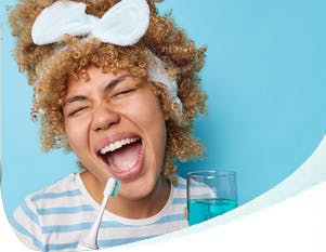 Smiling woman holding a toothbrush and a cup of mouthwash