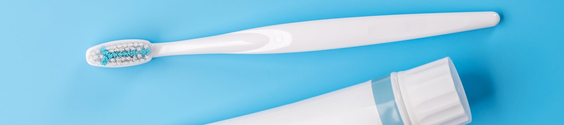 A white toothpaste tube and toothbrush against a blue background