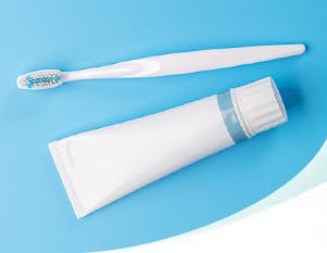 A white toothpaste tube and toothbrush against a blue background