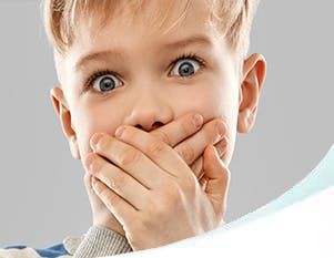 Blond boy in a striped shirt with wide eyes and his hands clamped over his mouth