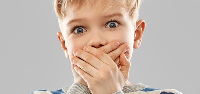 Blond boy in a striped shirt with wide eyes and his hands clamped over his mouth