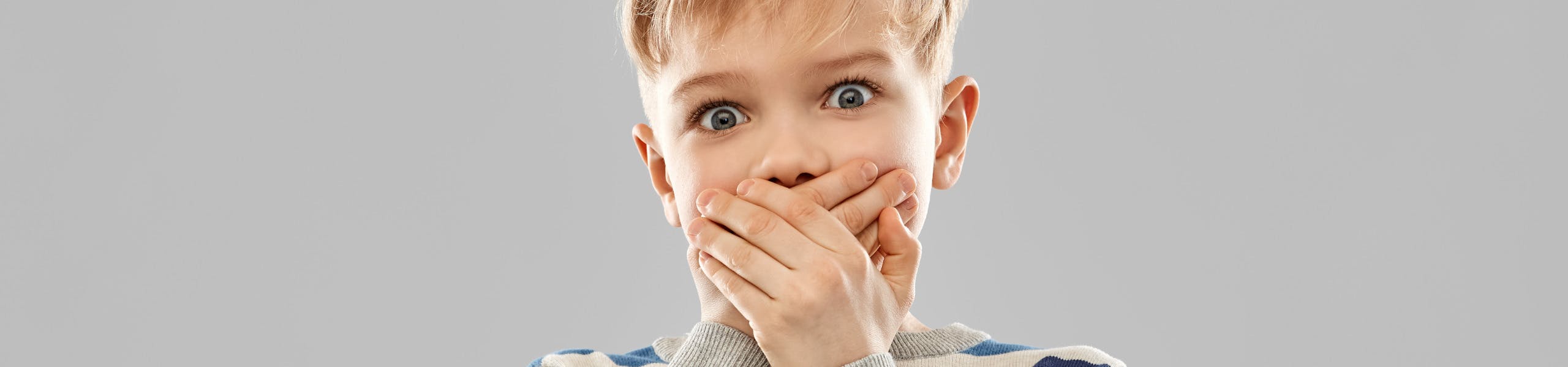 Blond boy in a striped shirt with wide eyes and his hands clamped over his mouth