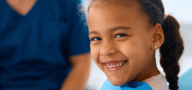 Young black girl sitting in a chair at the dentist’s office and smiling