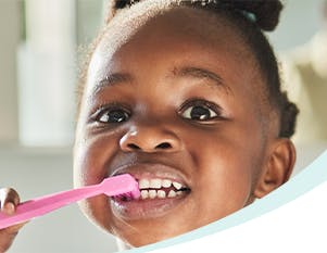 Cute African American toddler brushes her teeth with a pink tooth brush