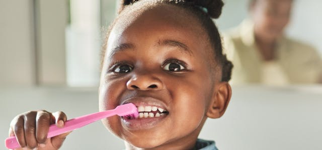 Cute African American toddler brushes her teeth with a pink tooth brush