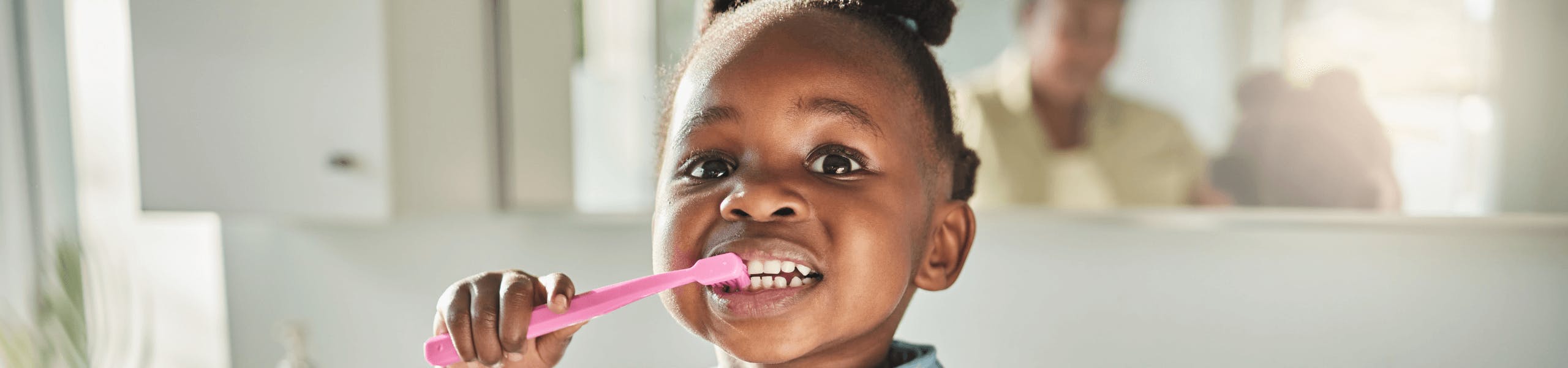 Cute African American toddler brushes her teeth with a pink tooth brush