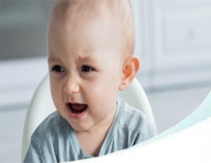 Crying baby turning away from a bottle in a highchair