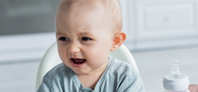Crying baby turning away from a bottle in a highchair