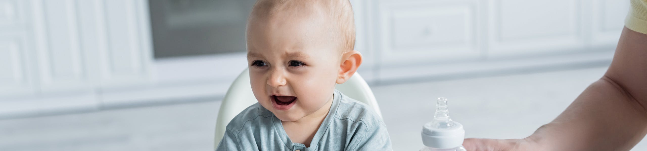 Crying baby turning away from a bottle in a highchair