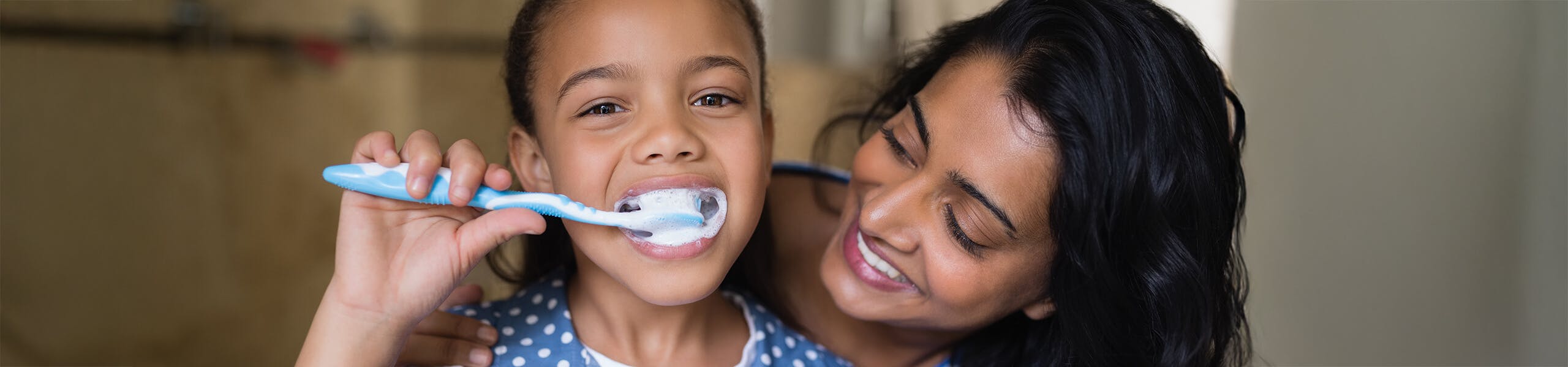A woman smiling while her daughter brushes her teeth