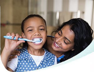 A woman smiling while her daughter brushes her teeth