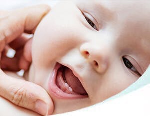 Baby lying on a bed, with bottom two teeth breaking through gums