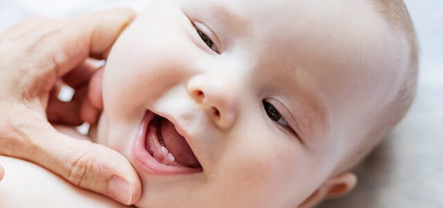 Baby lying on a bed, with bottom two teeth breaking through gums