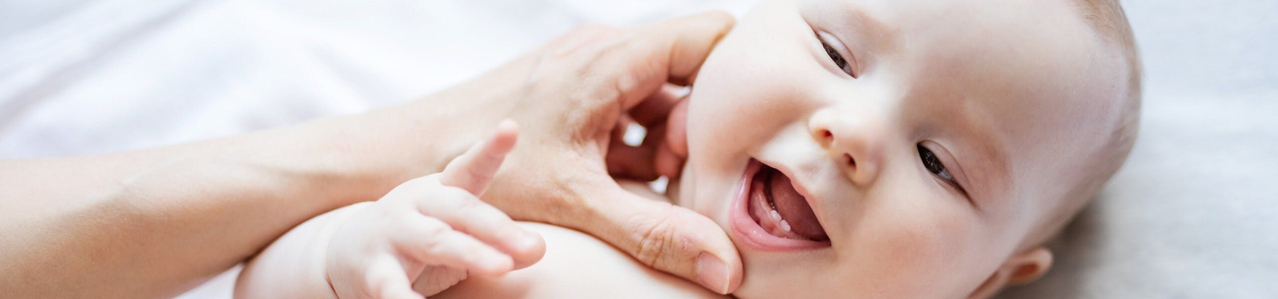 Baby lying on a bed, with bottom two teeth breaking through gums