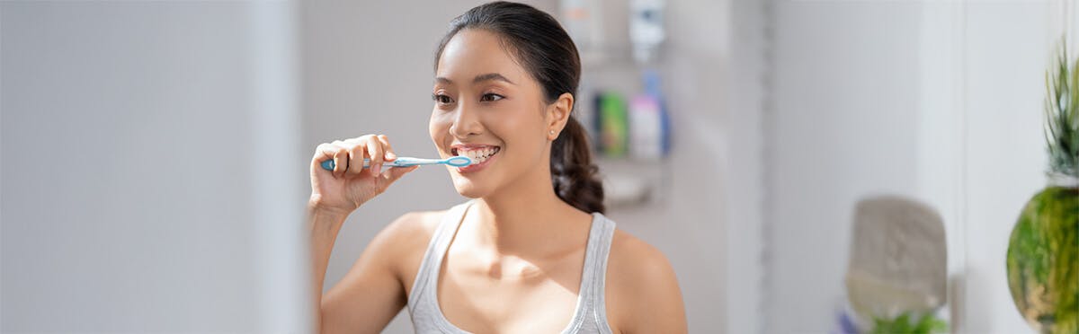 Woman brushing her teeth with a blue and white toothbrush