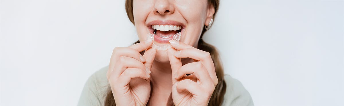 Smiling woman holds a clear aligner as though she’s just taken it out of her mouth