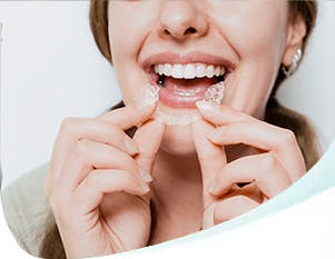 Smiling woman holds a clear aligner as though she’s just taken it out of her mouth