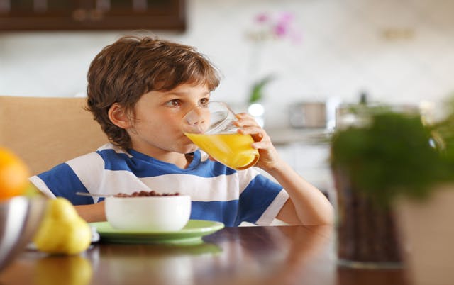 Jeune garçon buvant un grand verre de jus d'orange acide